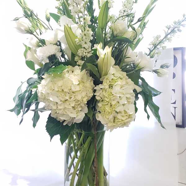 White floral arrangement in a tall glass vase with lilies and hydrangeas
