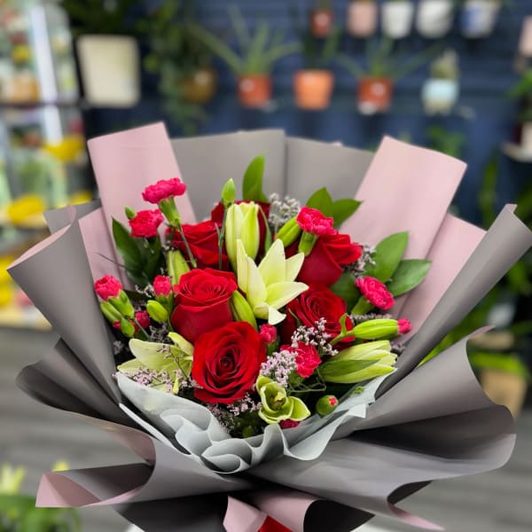 Bouquet of red roses, lilies, and pink carnations wrapped in gray and pink paper