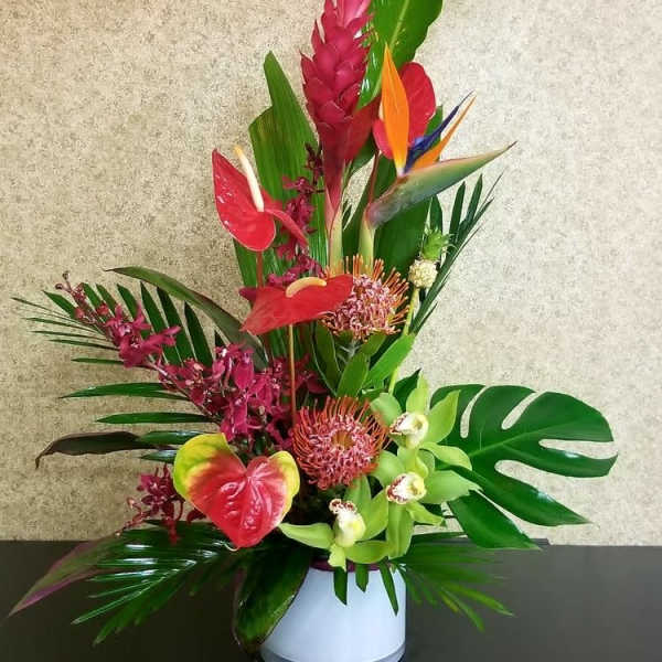 Tropical flower arrangement in a white vase with red and green blooms