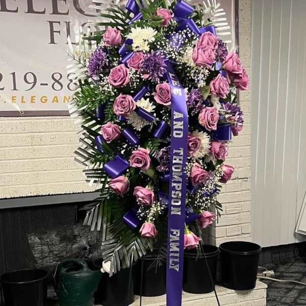 Standing sympathy spray with pink roses and purple flowers on an easel