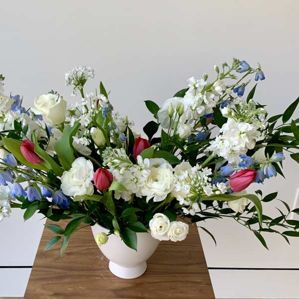 White and blue floral arrangement with pink tulips in a white vase