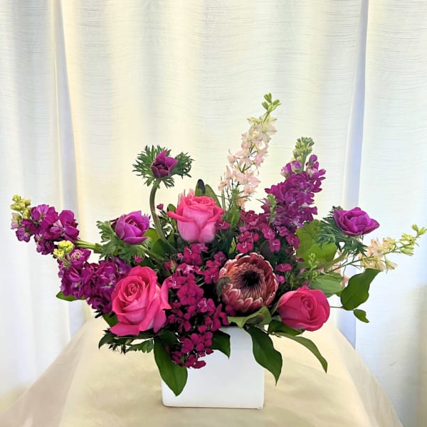 Pink and purple floral arrangement in a white square vase