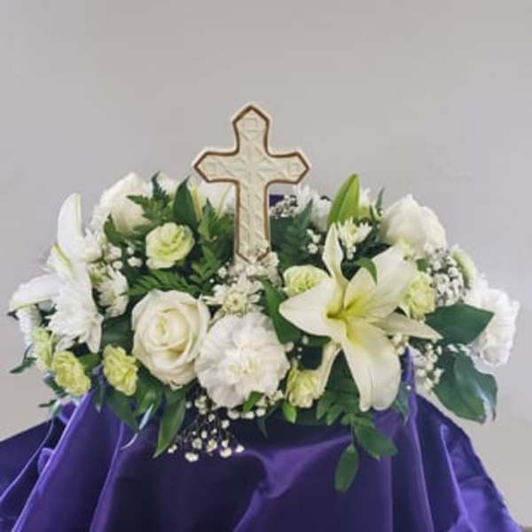 White floral arrangement with a cross centerpiece on purple cloth