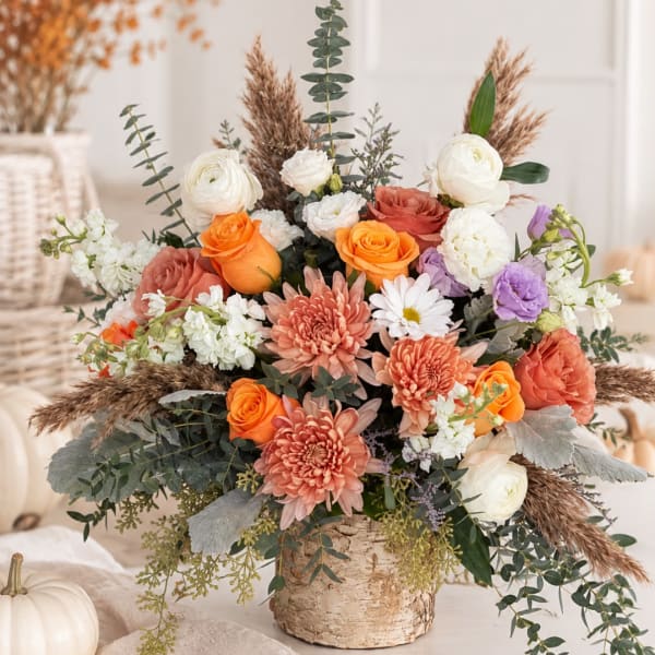 Mixed bouquet of orange, white, peach, and purple flowers in a birch vase