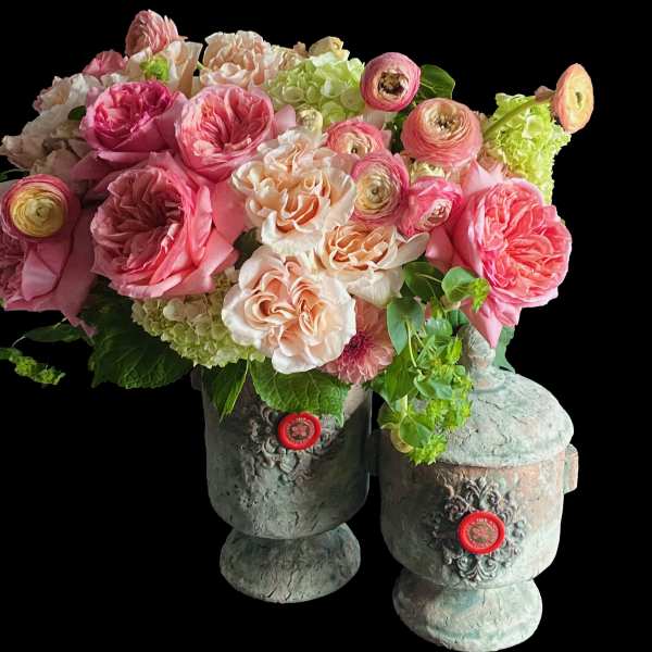 Lush arrangement of pink and peach roses, ranunculus, and hydrangeas in two rustic stone urn vases.