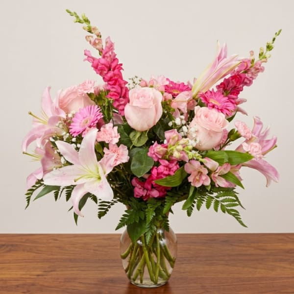 Pink lilies, roses, and gerbera daisies in a clear glass vase
