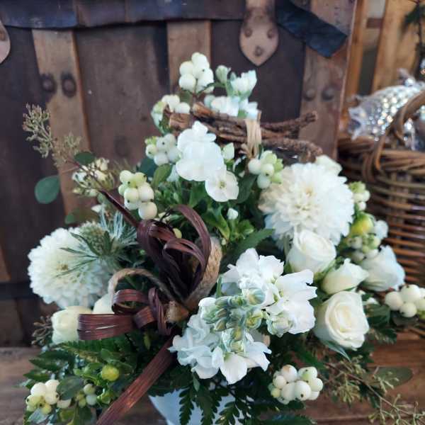 White floral arrangement in a white vase with berries and ribbon
