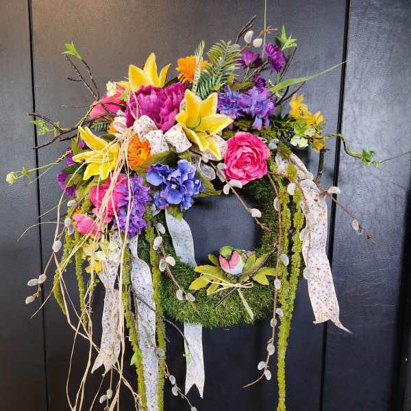 Colorful floral wreath with lilies, roses, and ribbons on a dark door