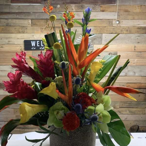Tropical floral arrangement in a textured vase with orange, red, yellow, and green blooms