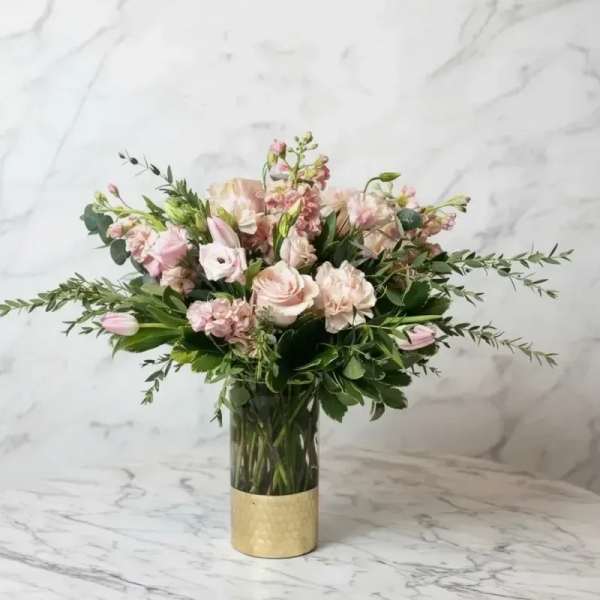 Pink and cream bouquet in a clear glass vase with a gold base