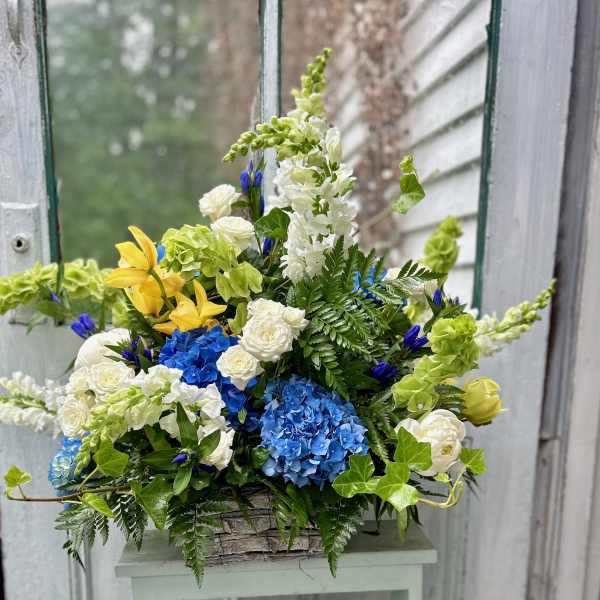 Mixed bouquet with blue hydrangeas, white roses, and yellow lilies in a basket