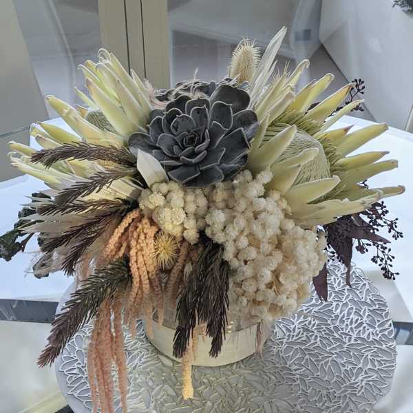 Succulent arrangement with pale cream blooms in a round container