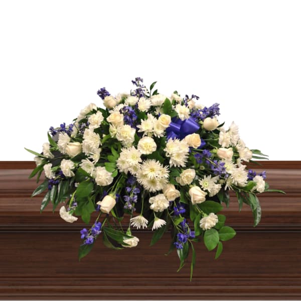Large white and purple floral spray on a wooden casket