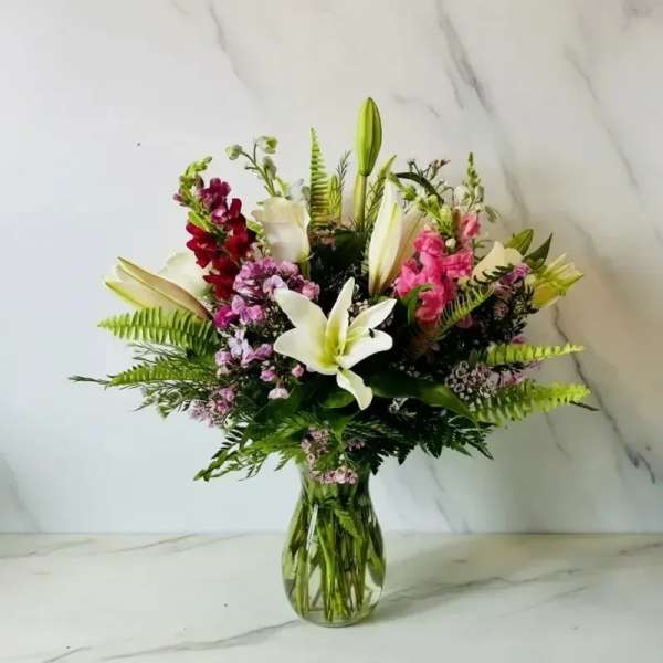 Mixed bouquet of lilies, snapdragons, and pink filler flowers in a glass vase