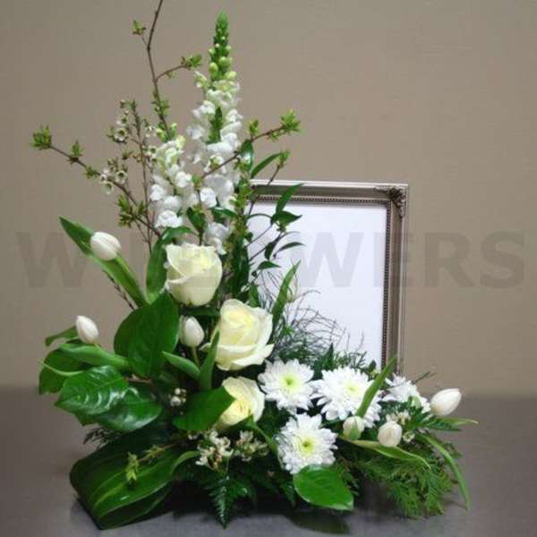 White floral arrangement with roses, tulips, and daisies in a framed display