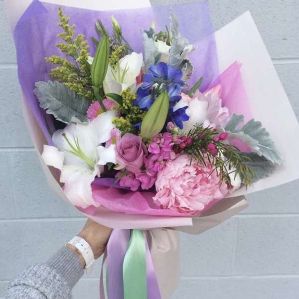 Handheld bouquet of pink, white, and blue flowers wrapped in pastel paper