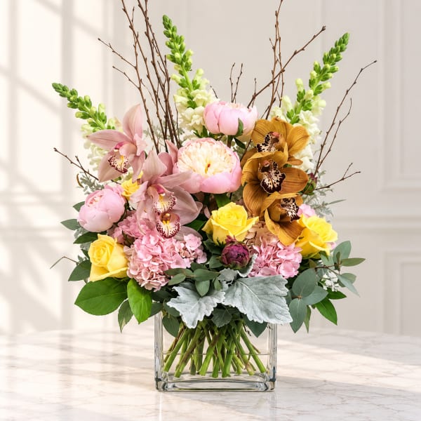 Mixed bouquet in a clear square vase with pink, yellow, and white blooms