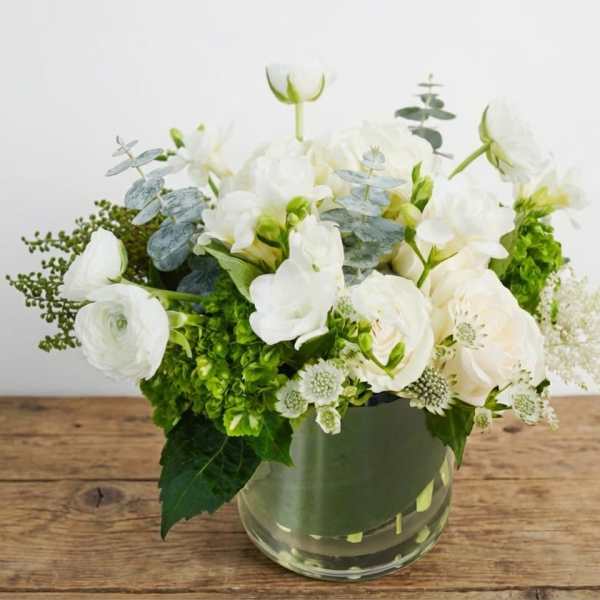 White flowers arranged in a clear glass vase with green accents