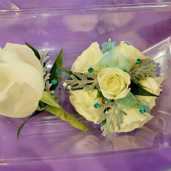 Two cream rose corsages in a purple plastic box