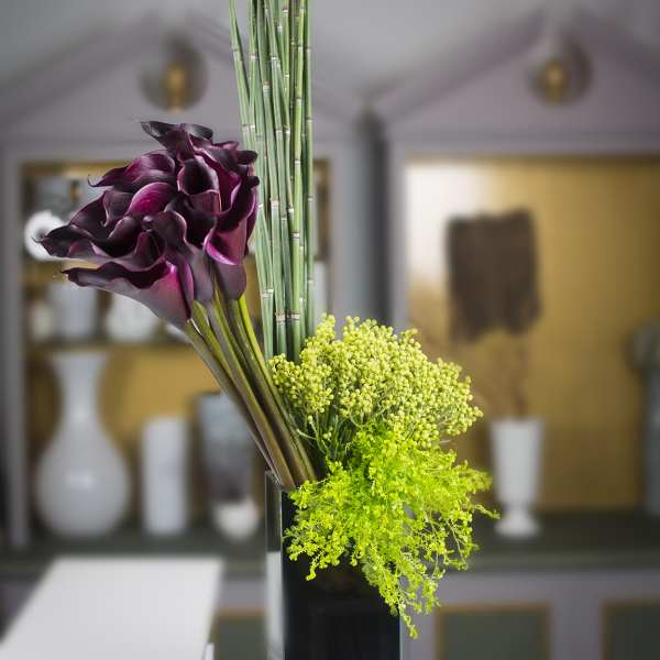 Purple calla lilies with green filler in a tall black vase