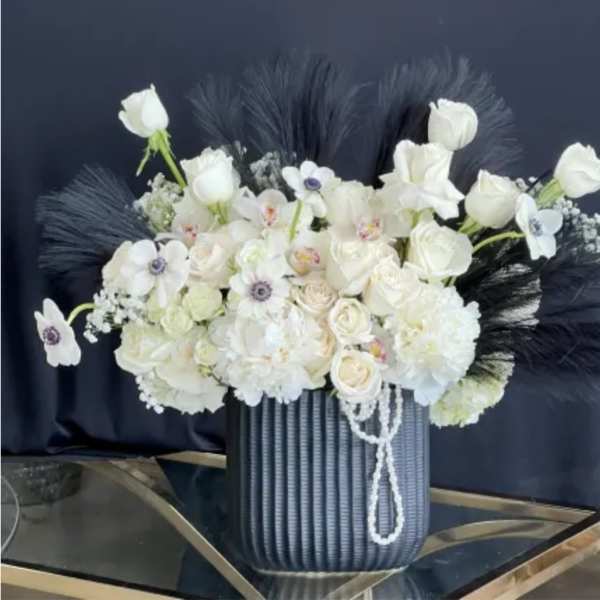 White floral arrangement in a ribbed blue vase with dark feather accents