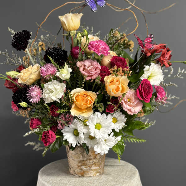 Mixed bouquet of roses, daisies, and carnations in a birch-style container