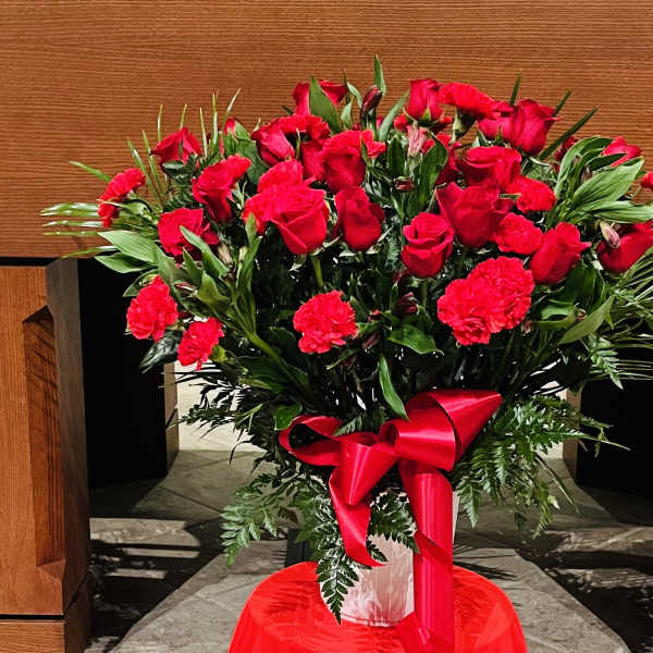 Red roses and carnations arranged in a vase with a red ribbon