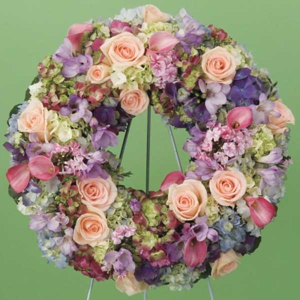 Circular floral wreath with pink roses and purple blooms on a stand