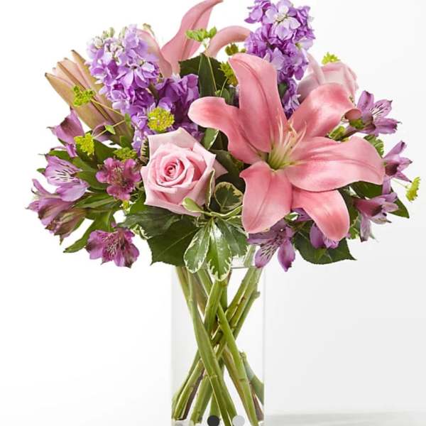 Pink lilies and roses with purple flowers in a clear glass vase