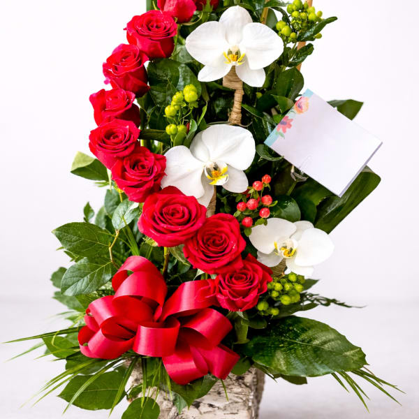 Red roses and white orchids in a square vase with a red ribbon