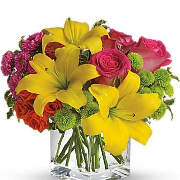 Bouquet of yellow lilies, pink roses, and green button mums in a clear square vase