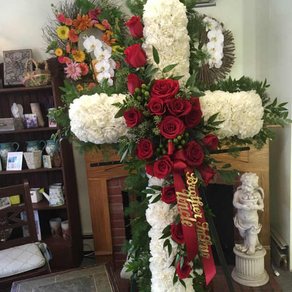 Large funeral cross of white flowers and red roses with a ribbon