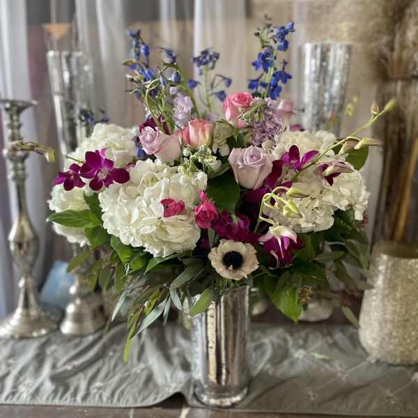 Mixed bouquet of white hydrangeas, pink roses, and purple orchids in a silver vase