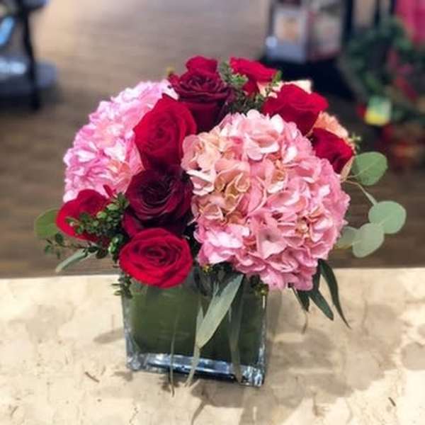Red roses and pink hydrangeas in a square glass vase