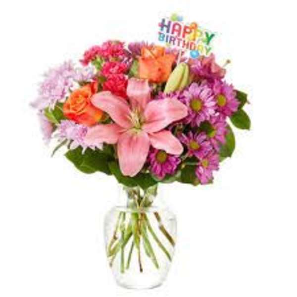 Colorful mixed bouquet in a clear glass vase with a birthday sign