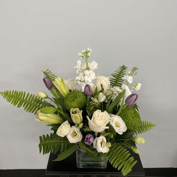White and purple floral arrangement in a glass vase with green accents