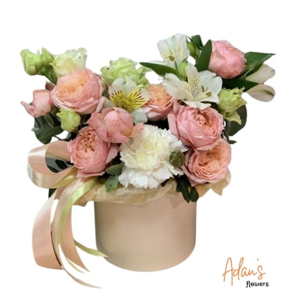 Pink and white flower arrangement in a round beige box with ribbon
