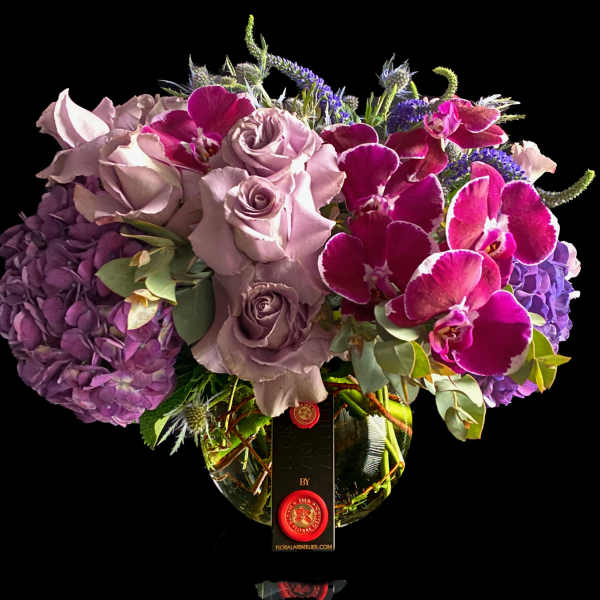 Bouquet of lavender roses, purple hydrangeas, and magenta orchids in a glass vase