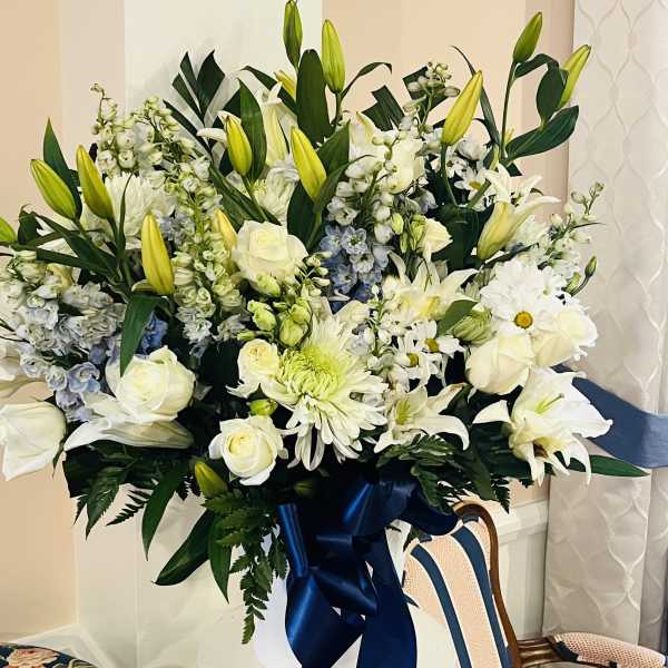 Large white floral arrangement with lilies and roses in a vase with a blue ribbon