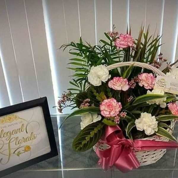 Pink and white carnations in a white basket with a pink ribbon