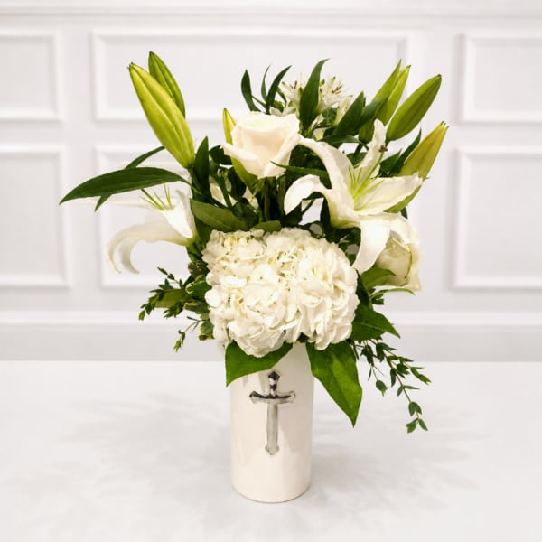 White lilies and hydrangea in a white vase with a cross emblem