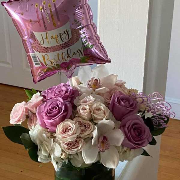 Pink birthday balloon above a vase of pink and white roses and orchids