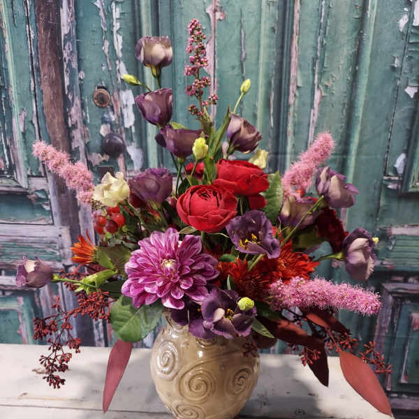 Mixed bouquet of red, purple, and pink flowers in a beige vase