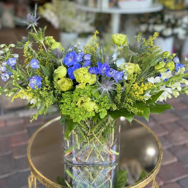 Mixed bouquet of blue, green, and white flowers in a clear glass vase