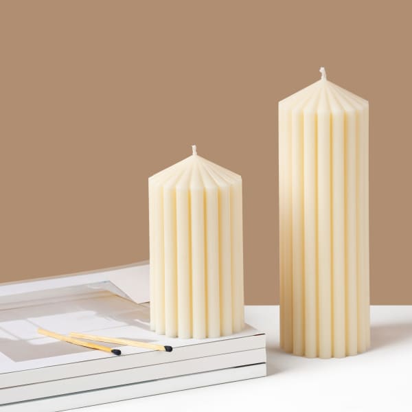 Two cream pillar candles on a white surface with matches nearby