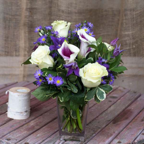 Bouquet of white roses, purple calla lilies, and small purple daisies in a glass vase