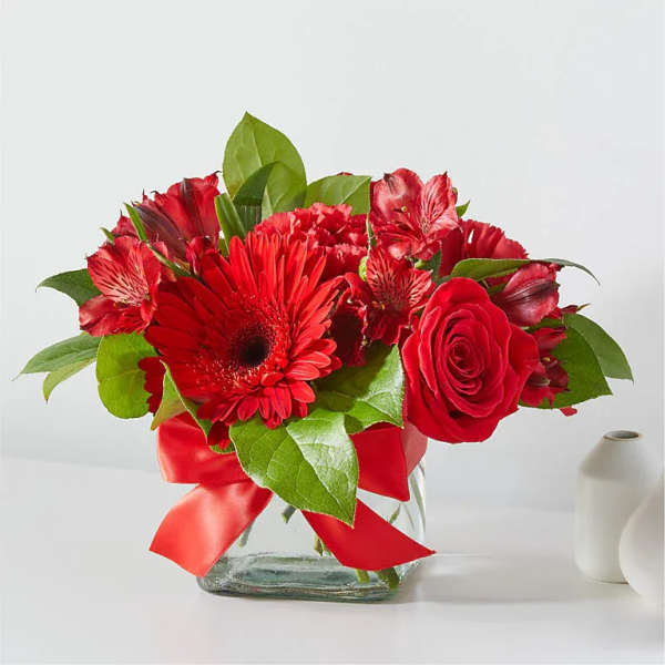 Red flowers arranged in a glass vase with a red ribbon