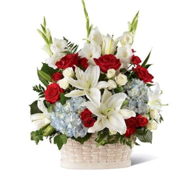 Patriotic basket arrangement with white lilies, red roses, and light blue hydrangeas in a white woven basket