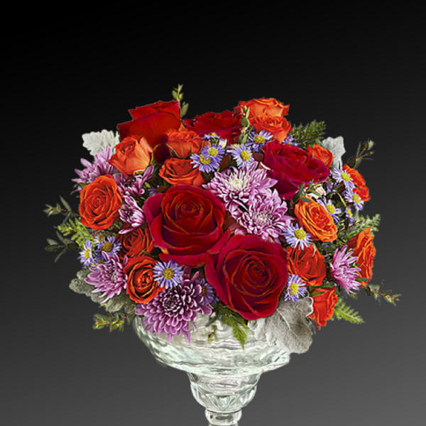 Mixed bouquet of red and orange roses with purple daisies in a clear glass vase