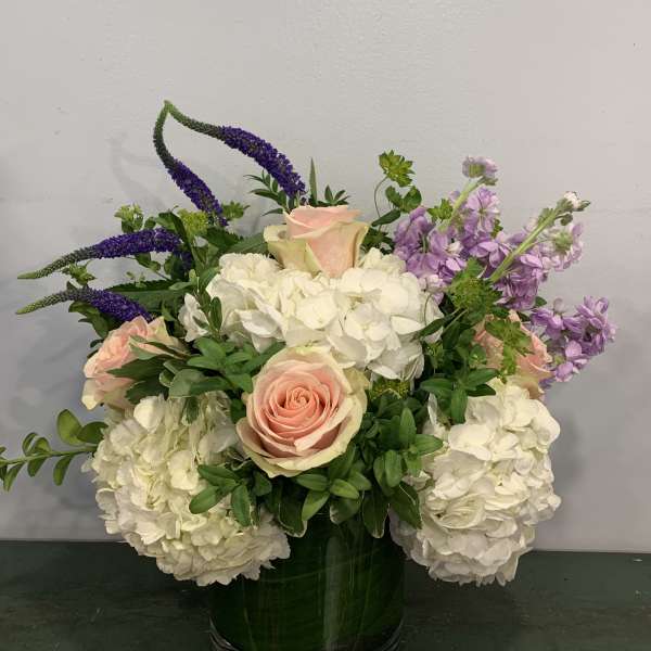 Pink roses with white hydrangeas and purple spikes in a glass vase